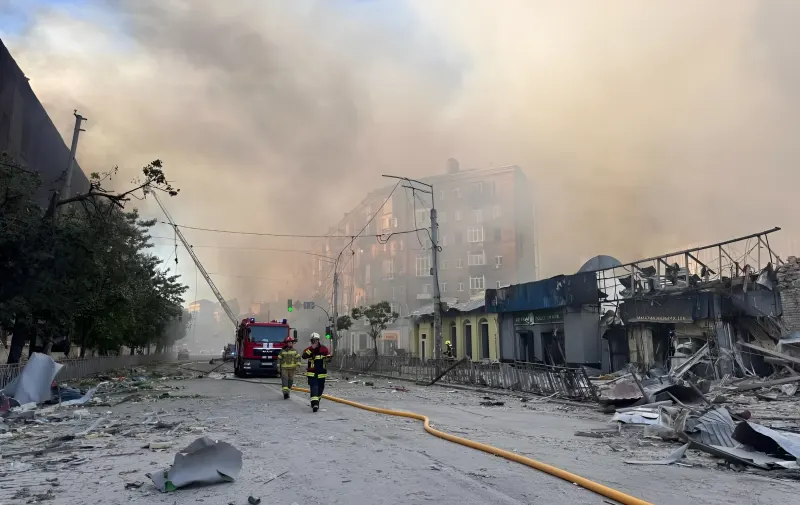 Пожарные тушат пожар на улице Киева после ракетного удара, на фоне видны разрушенные здания и дым