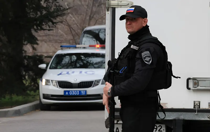 Российский полицейский с автоматом стоит на посту у дороги, на фоне видна машина ДПС и грузовик