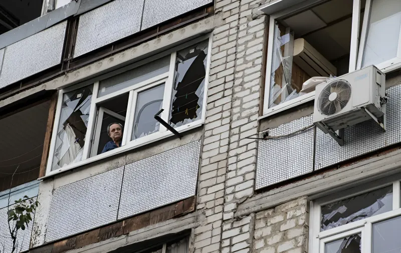 Пошкоджений фасад житлового будинку в Богодухові після російського обстрілу, збиті вікна та людина на балконі
