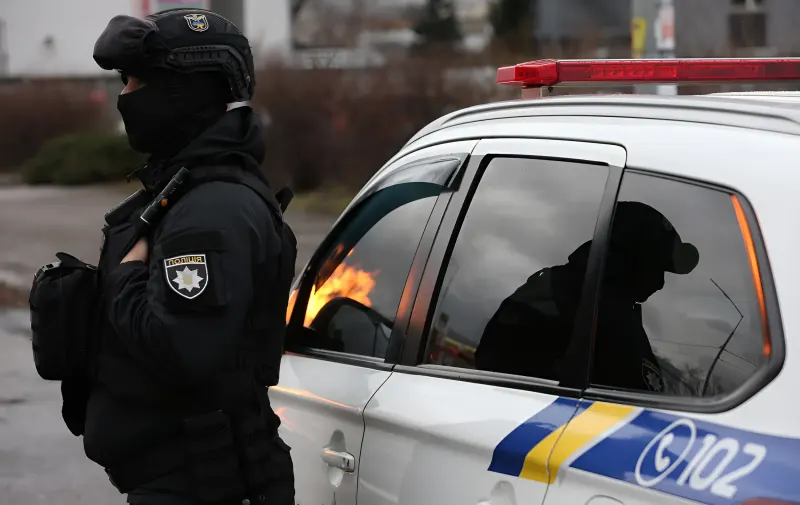 Поліцейський у тактичному обладнанні стоїть біля патрульного автомобіля на фоні пожежі після обстрілу в Києві