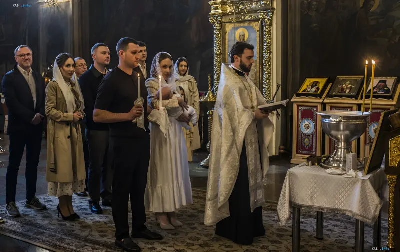 Крещение ребенка в церкви: священник проводит таинство, а крестные родители держат свечи рядом с младенцем