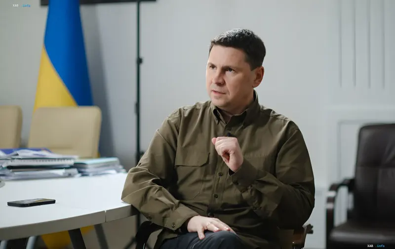 Владимир Зеленский в военной форме, сидящий за столом с украинским флагом на фоне — символ решимости Украины в ответ на угрозы со стороны Беларуси