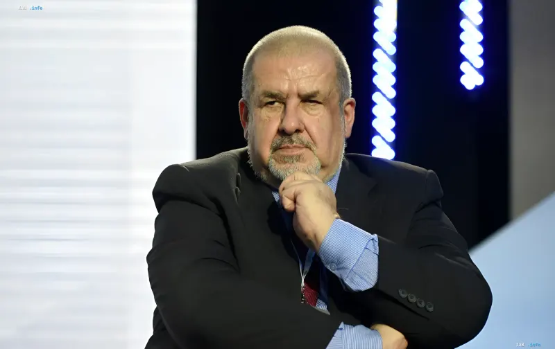 Рефат Чубаров в деловом костюме на фоне экрана с графикой, обсуждающий ситуацию в Крыму