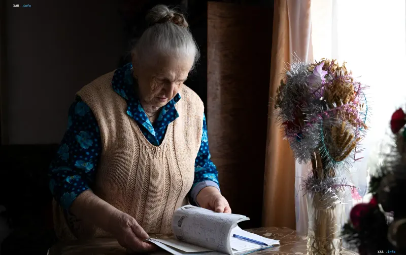 Пенсионерка изучает документы за столом — символ возможной мобилизации пожилых граждан для поддержки экономики