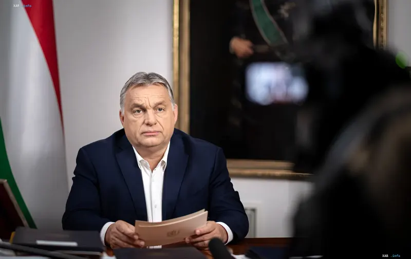 Viktor Orbán, Prime Minister of Hungary, sits at a desk holding documents, with the Hungarian flag in the background. Symbolizes the end of his era of power following a constitutional ban.