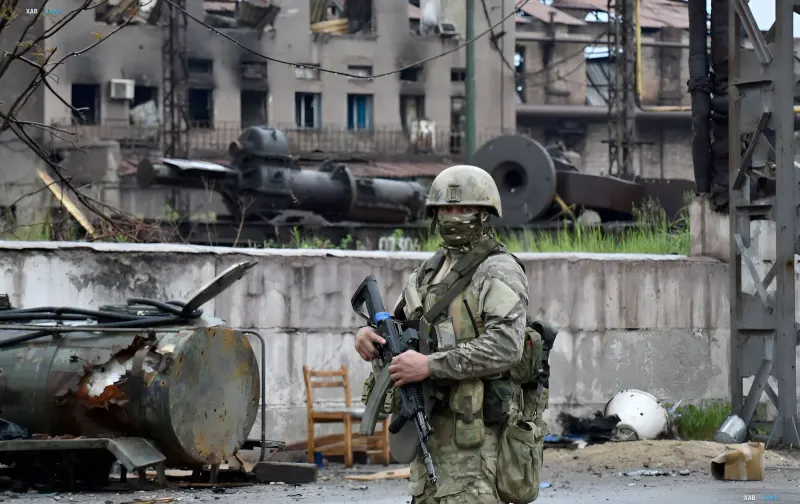 Украинский военнослужащий в камуфляже с автоматом на фоне разрушенного здания и военной техники на Херсонщине — символ последствий оккупации и угрозы биологического терроризма