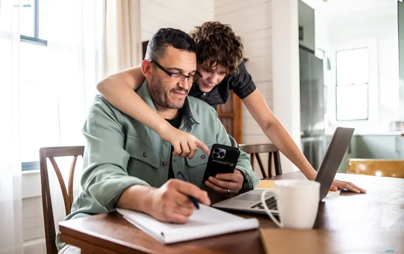 Father and son use smartphone and laptop to transfer child to school online as part of digitalization of education in Kyiv