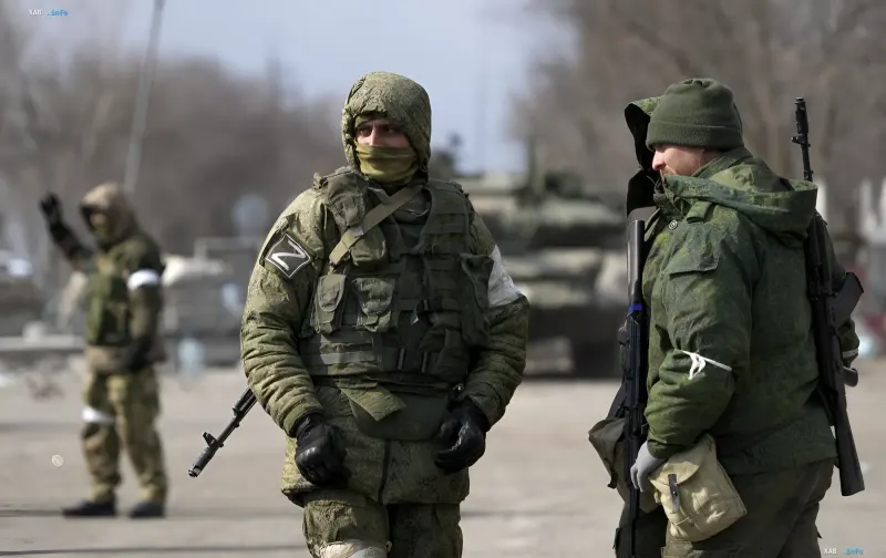 Російські військові з літерою Z на рукавах стоять на дорозі в Харківській області, на фоні видно бронетехніку
