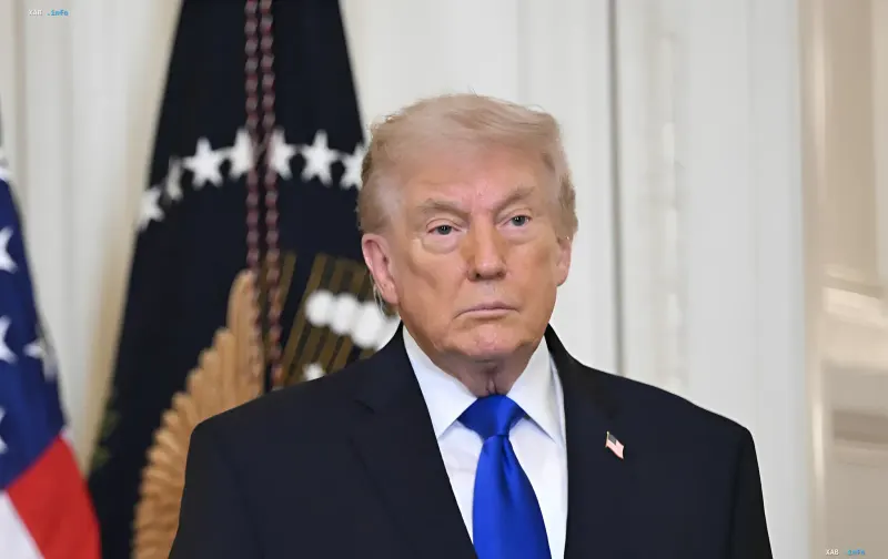 Дональд Трамп у офіційному середовищі з прапорами США на фоні, що символізує його рішучість ввести 100% тарифи на цифрові податки