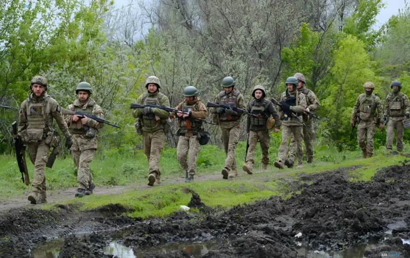 Ukrainian soldiers in camouflage uniforms and helmets with rifles in hand walk along a forest path, symbolizing the fight against the enemy in the context of new payments for captives