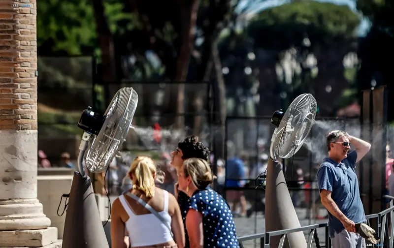 Tourists in Rome seeking relief from extreme heat under industrial misting fans near ancient ruins