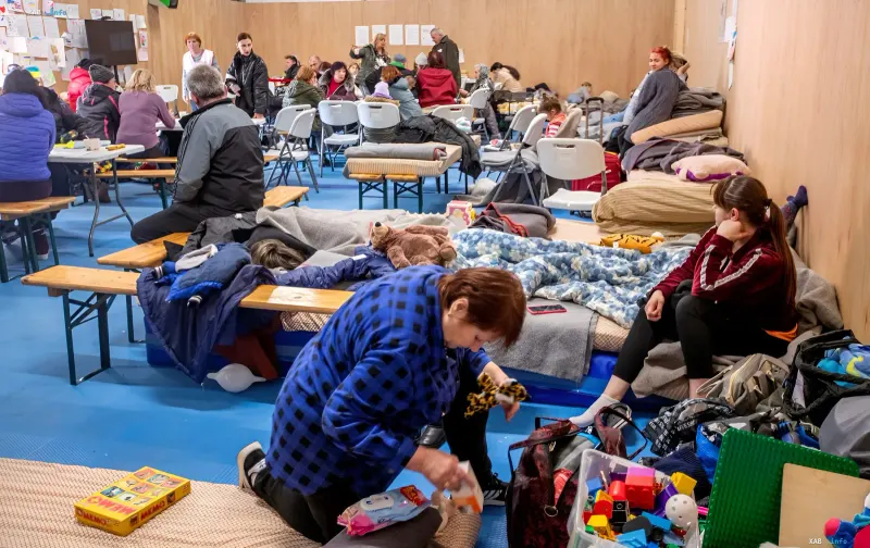 Ukrainian refugees in a temporary shelter: women and children resting on mattresses surrounded by belongings