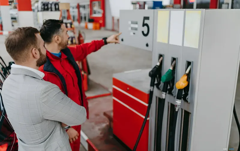 Gas station employee in red uniform explains fuel equipment operation to customer at a refueling station in Sumy region — part of gasoline supply system under shelling conditions