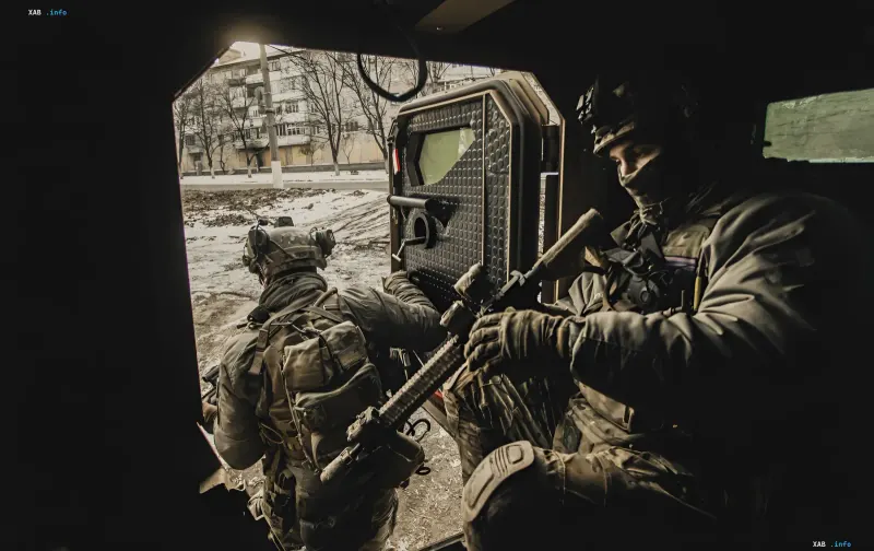Украинские военные в бронежилетах и шлемах с оружием в руках выходят из бронетранспортера, готовясь к операции на фоне зимнего пейзажа.