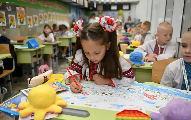 Erstklässlerin in traditioneller ukrainischer Vyshyvanka zeichnet im Klassenzimmer, was den Schuljahresbeginn und staatliche Unterstützung für Schulbedarf symbolisiert
