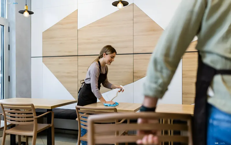 Junge Kellnerin reinigt Tische in einem modernen Café, illustriert Sommerjobs für Teenager in der Ukraine 2026