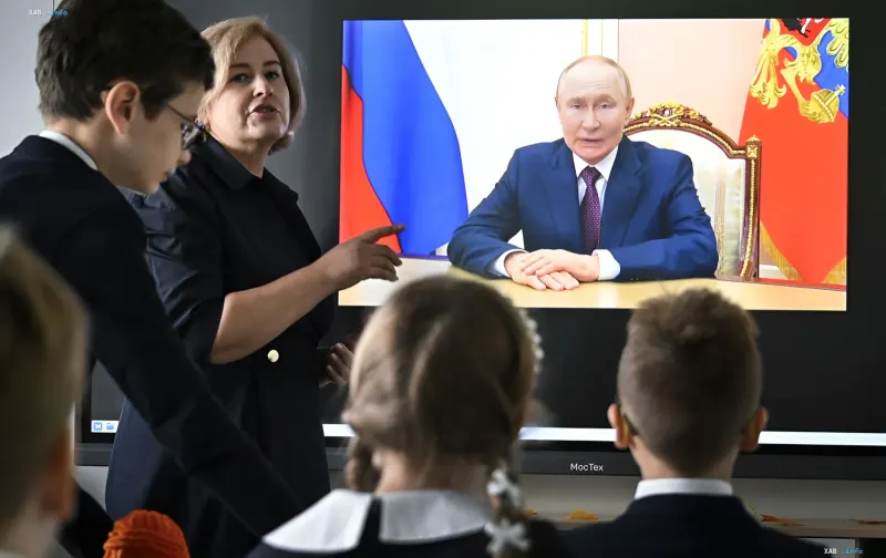 School lesson with Putin broadcast on screen: children and teacher watching a propaganda spectacle
