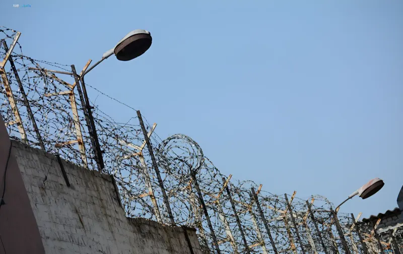 Stacheldrahtzaun und Straßenlaternen vor einem klaren Himmel, die die Folterorte in Oleniwka, Pakino und Taganrog symbolisieren, für die die EU Sanktionen gegen 23 Personen und eine Struktur verhängt hat.