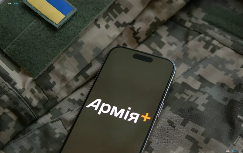 Смартфон с логотипом приложения «Армия+» на фоне военной формы с украинским флагом — символ цифрового военного билета