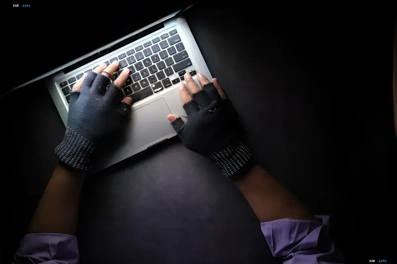 Hacker’s gloved hands typing on a laptop in darkness — metaphor for HalluSquatting attack where AI hallucinations turn user devices into botnets