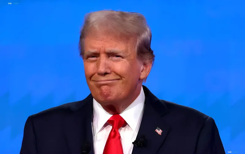 Donald Trump in a business suit with an American flag pin, smiling against a blue backdrop — illustrating the article about Trump’s shift in support for Zelenskyy