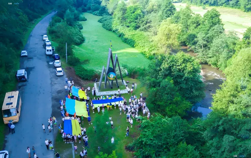 Kinder und Erwachsene mit ukrainischen Flaggen nahe einem Denkmal im Wald in Zakarpattien — wo Eltern über schlechte Bedingungen im Lager 'Artek' klagen