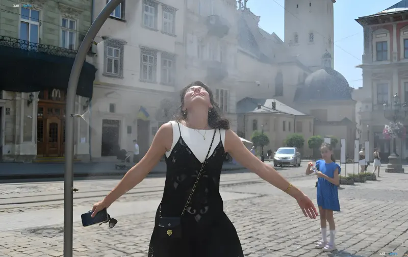 Frau genießt einen erfrischenden Brunnen auf einem Stadtplatz in der Ukraine während extremer Hitze von +38°C