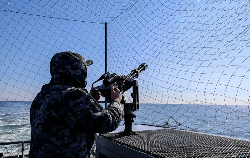 Моряк ВМС Украины в камуфляже управляет зенитным пулеметом на палубе корабля в Черном море — символ защиты от российских дронов после удара по «Сивашу»