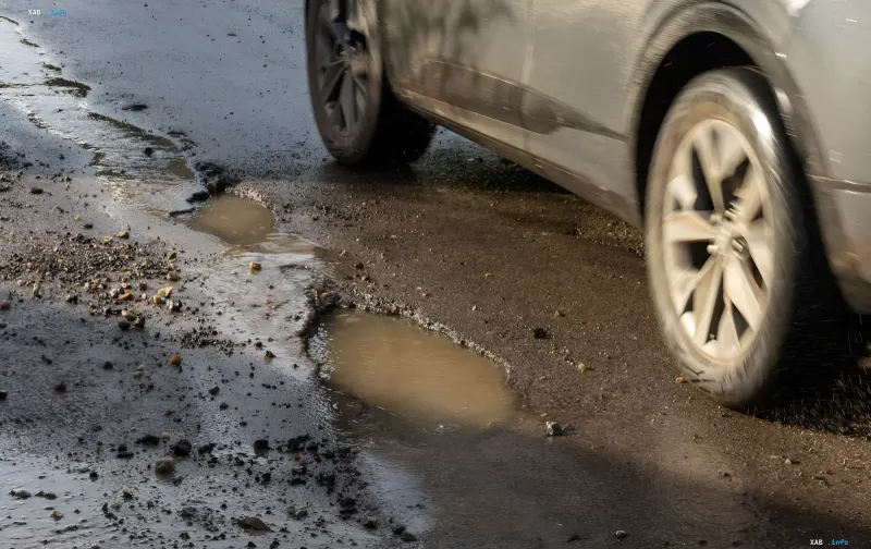 Автомобиль едет по дороге с глубокими ямами и лужами, что может привести к повреждению подвески — актуальная проблема для получения компенсации в 2026 году