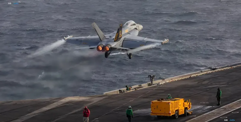 Истребитель F/A-18 Hornet взлетает с палубы авианосца ВМС США на фоне штормового моря, иллюстрируя напряженную ситуацию с логистикой и нехваткой экипажей на Ближнем Востоке