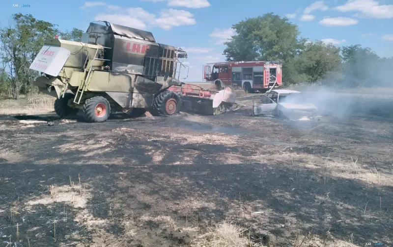 Burnt Claas combine harvester and car after drone strike in Zaporizhzhia region, fire trucks at the scene