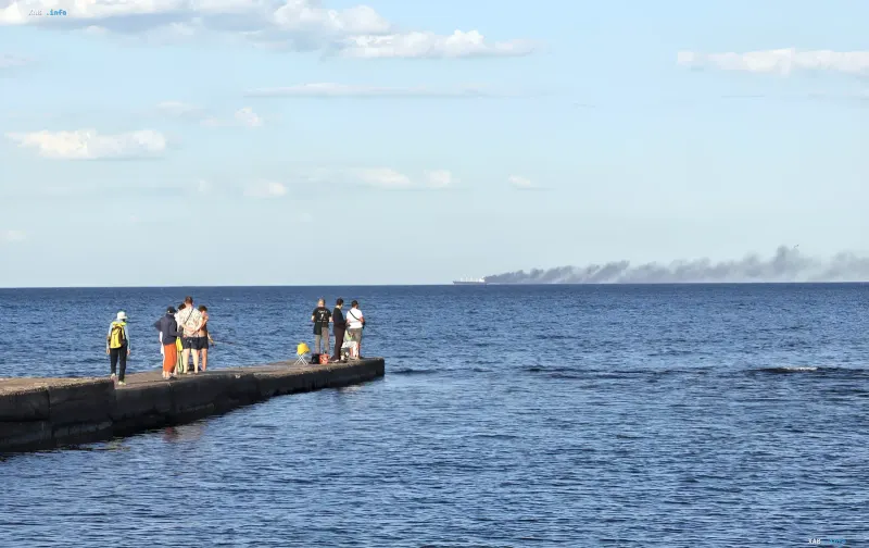 A group of people on a pier observes smoke from a distant ship, symbolizing threats to the grain corridor and the role of the Ukrainian Navy in its protection in 2026