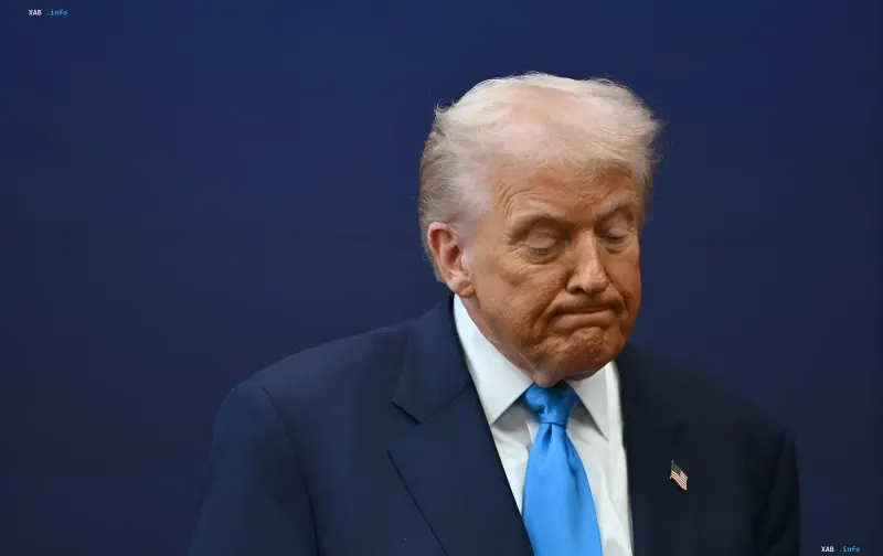 Дональд Трамп с грустным выражением лица на фоне синей стены, отражающий падение рейтинга из-за войны с Ираном и экономического кризиса