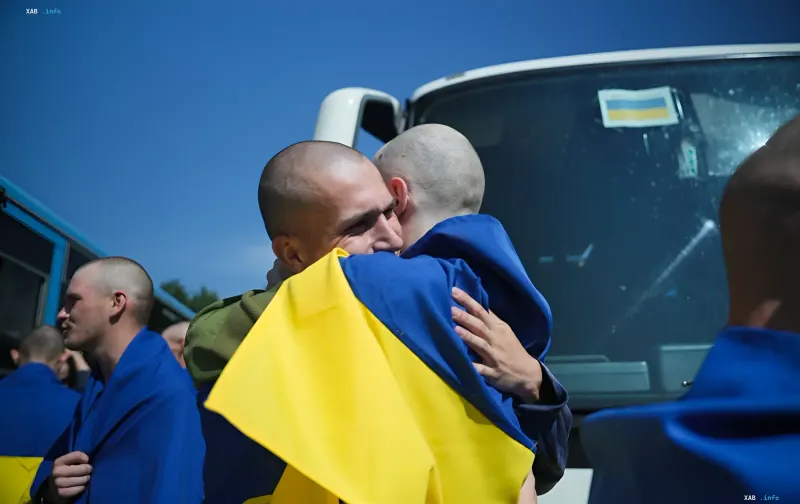 Ukrainian soldiers embrace after returning from captivity as part of the 77th prisoner exchange, holding the Ukrainian flag