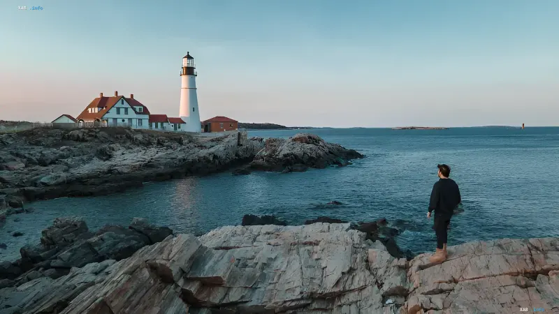 Felsige Küste von Eastport in Maine: Eine Person steht auf den Felsen am Wasser und blickt auf den Leuchtturm — diese Ufer schützen die Anwohner vor dem DeepGreen-Projekt eines Unterwasser-KI-Rechenzentrums, das ein 180-tägiges Moratorium auslöste