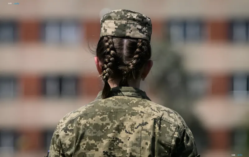 Frau in digitaler Tarnuniform mit Zöpfen vor Kasernen — Illustration zur Meldung, dass die Rada die Vorbereitung der Mobilisierung von Frauen in der Ukraine dementiert