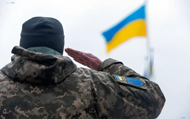 Украинский военный в камуфляже отдает салют украинскому флагу на фоне новости об упрощенном возврате из СЗЧ