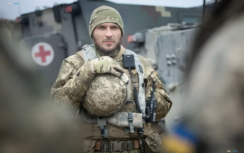 Ukrainian soldier in camouflage holding a helmet in front of military vehicles during counteroffensives in Sumy and Kharkiv regions