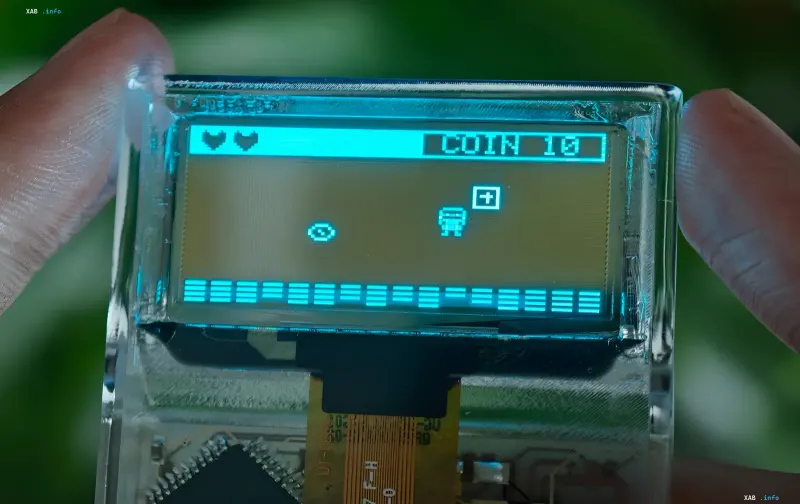Transparente Retro-Konsole Arduview im Hosentaschenformat mit sichtbarer Platine und OLED-Display, auf dem ein Pixel-Art-Spiel läuft