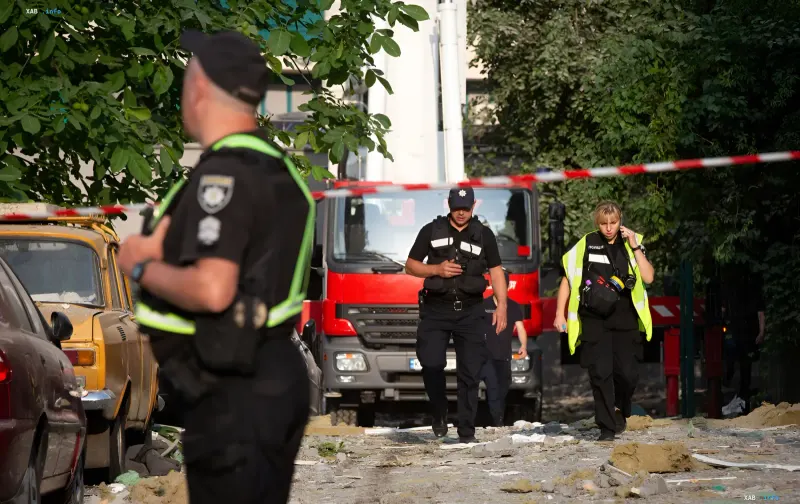 Streifenpolizei am Ort eines Raketenangriffs in Kyjiw: Beamte hinter dem Absperrband neben beschädigten Autos und Rettungsfahrzeug