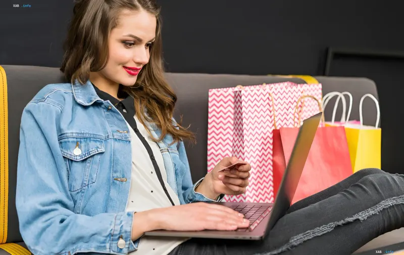 Frau plant Herbst-Online-Shopping im September 2026: hält eine Bankkarte, arbeitet am Laptop, daneben Einkaufstüten
