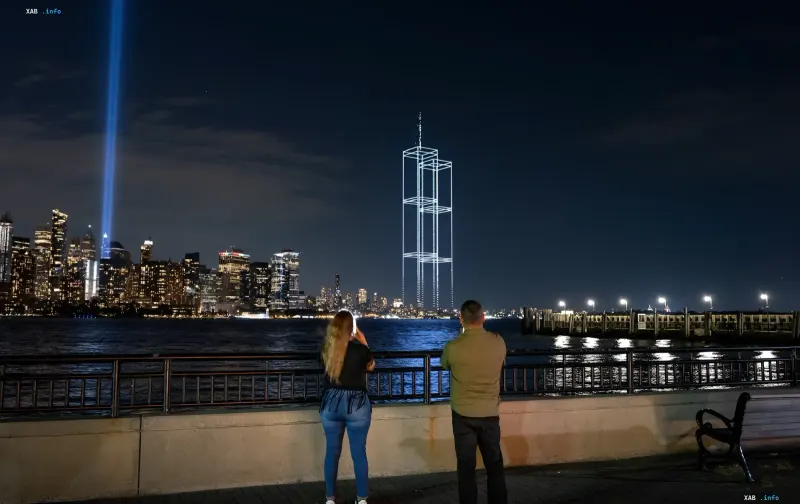 Drone light show recreating the Twin Towers over New York Harbor for the 25th anniversary of 9/11; onlookers watch and film from the waterfront