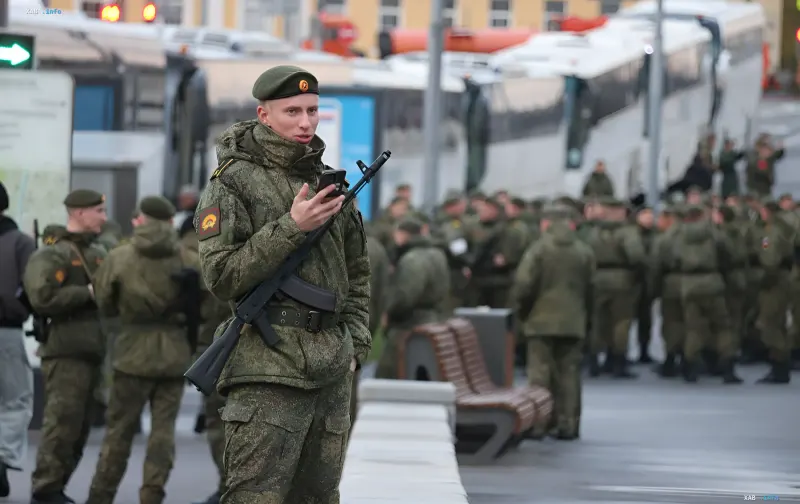 Russischer Soldat mit AK-Gewehr in Tarnkleidung vor einer Menschenmenge aus Soldaten und Bussen — der Preis des Kriegsfür Russland