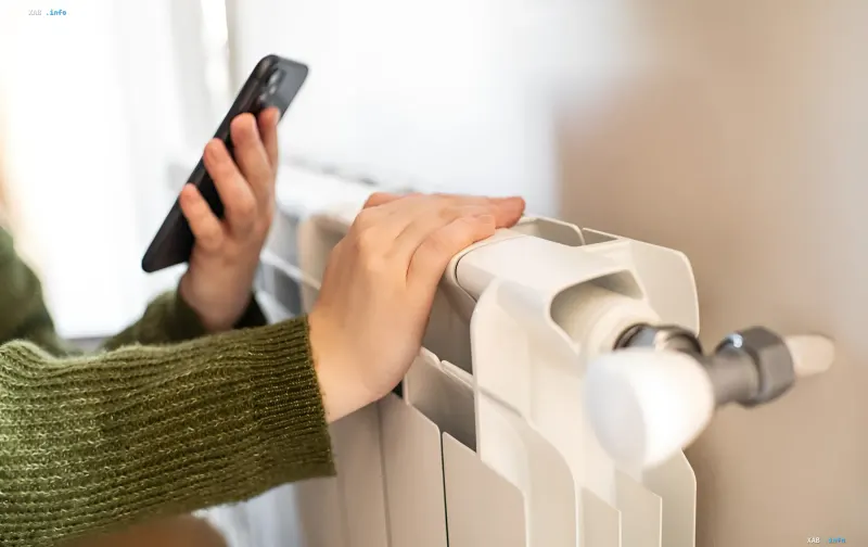Frau prüft die Temperatur der Heizungsheizung und nutzt ein Smartphone zur Dokumentation des Problems