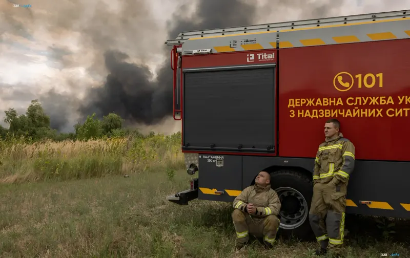 Feuerwehrleute ruhen neben einem Feuerwehrauto mit Rauch aus einem brennenden Feld in der Region Schytomyr