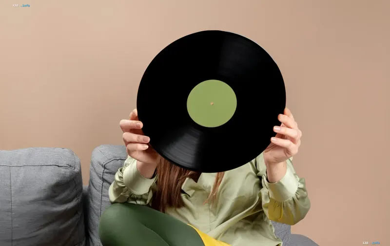 A woman hides her face behind a vinyl record against a grey sofa, illustrating the upcoming Vinyl Market in Kyiv