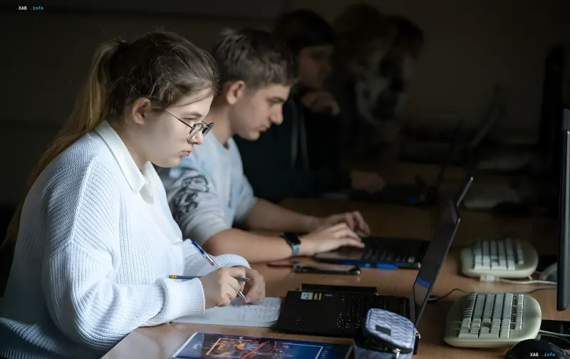 High school students in a computer lab: a girl takes notes in a notebook while a boy works on a laptop, illustrating the new profile-based model of senior secondary education in Ukrainian lyceums