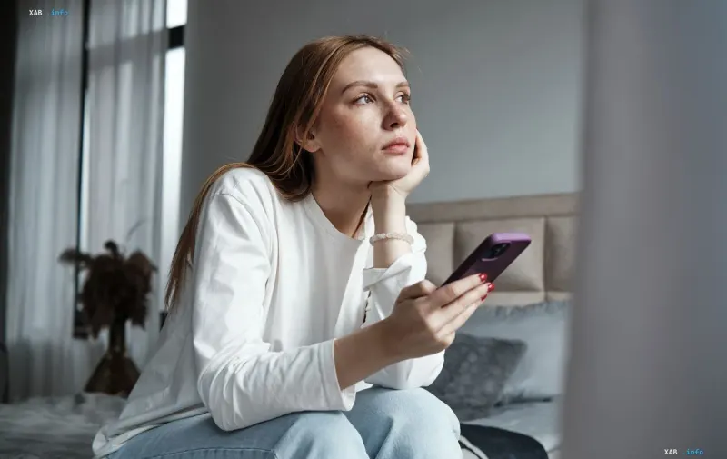 Frau mit Smartphone in der Hand, die nachdenklich in die Ferne blickt, symbolisiert Internetausfälle in Kiewer Haushalten nach dem Angriff