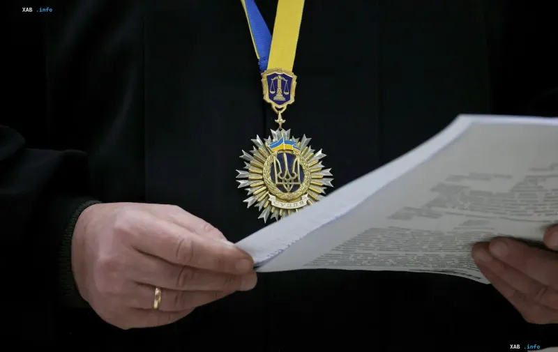Richterliche Auszeichnung mit dem Wappen der Ukraine und der Waage der Gerechtigkeit auf der Brust einer Person in Schwarz, die Dokumente hält — visueller Kontext des von NABU aufgedeckten Richter-Netzwerks