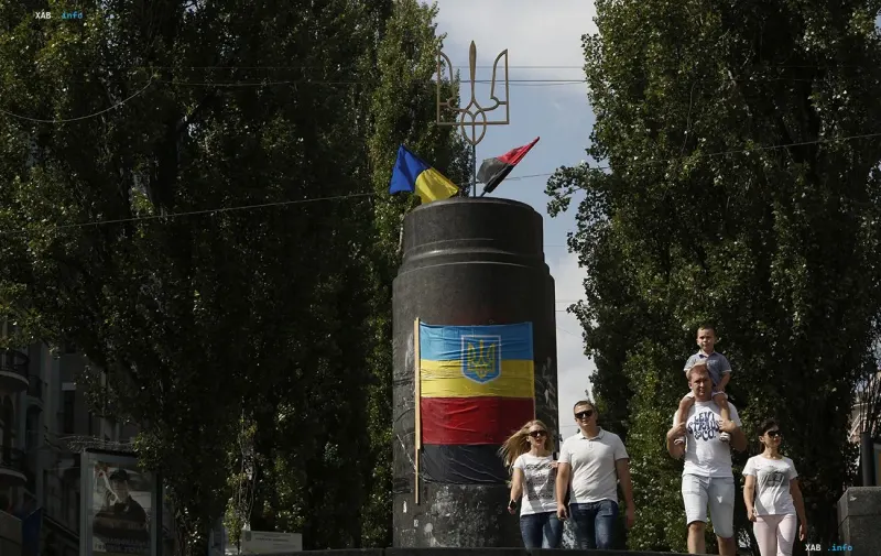 A monument with the Ukrainian coat of arms and trident in central Kyiv, with pedestrians walking by